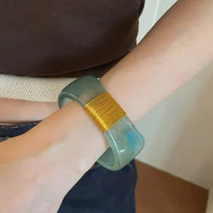 Close-up of a wide resin bangle featuring a marbled swirl and gold wire-wrapped detail