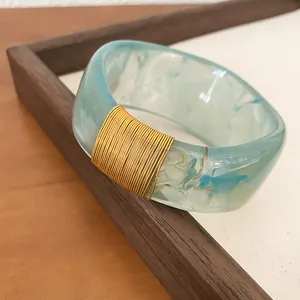 Detailed shot of marbled light blue resin bangle with elegant gold wire-wrap accent.