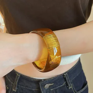 Close-up of a wide amber marbled resin bangle with gold wire wrap on a wrist.