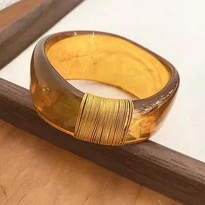 Close-up of a wide translucent amber resin bangle featuring an elegant gold wire-wrapped detail