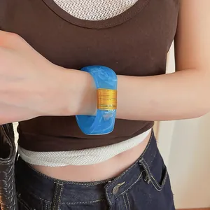 Detailed view of a wide blue marbled resin bangle with elegant gold wire wrap on wrist