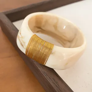 Macro detail of a wide marble resin bangle featuring a sophisticated gold wire wrapped section