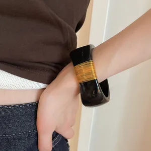 Detail shot of a wide black resin bangle with elegant gold wire wrapping worn on a wrist
