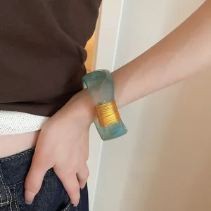 Detailed view of a wide marbled resin bangle with elegant gold wire wrapping on a model.
