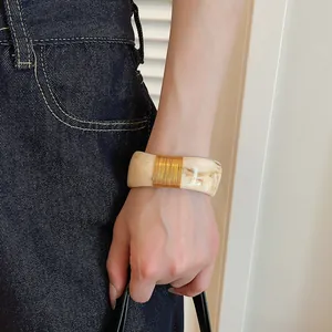 Close-up detail of a marbled resin wide bangle with elegant gold wire wrap on a wrist