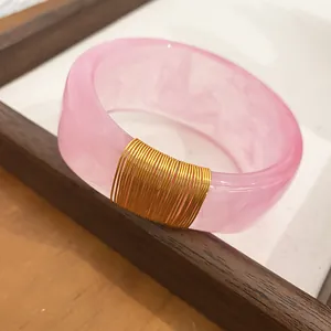 Close-up of pink marbled resin bangle with elegant gold wire wrap detail