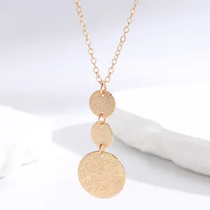 Close-up of golden tiered round pendants with pebbled texture on a thin chain.