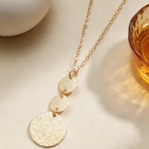 Detailed view of gold geometric necklace with three textured round metal disc pendants.