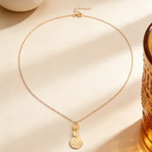Close-up of gold tiered disc pendant necklace on warm neutral background