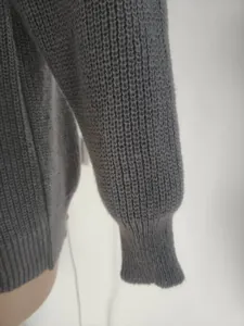 Close-up of grey knitted sweater sleeve showing thick ribbed texture and cuff detail.