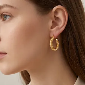 Nahaufnahme eines 18K vergoldeten gedrehten Creolen-Ohrrings, getragen von einem Modell