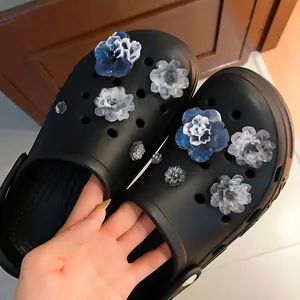 Elegant blue and white floral shoe charms decorating black garden clogs in detail view.