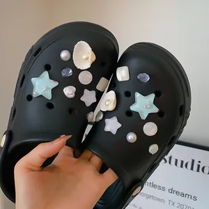 Close-up of DIY shoe charms featuring pearls and shells on black clogs