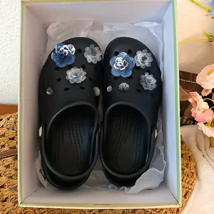 Close-up of elegant floral charms and resin flower decorations on black clogs in a gift box
