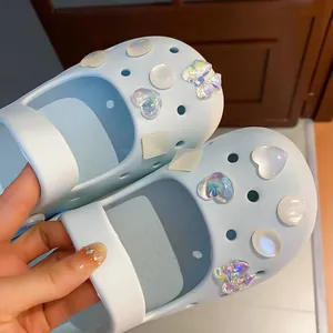 Close-up view of iridescent bow and pearl heart charms on light blue clog shoes decoration