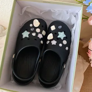 Close-up of elegant pearl and shell charms on black clogs in a gift box