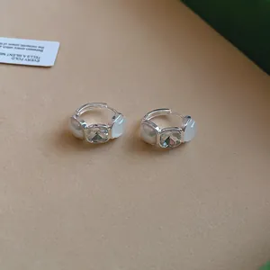 Primer plano de pendientes de aro plateados con cristal y perlas blancas.