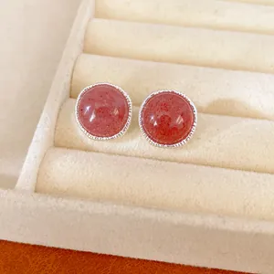Close-up detail of round pink stone stud earrings with a textured silver border design