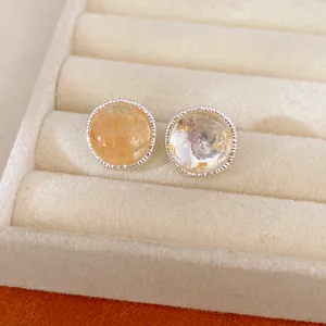 Close-up detail of elegant round stud earrings featuring amber stones and silver textured borders