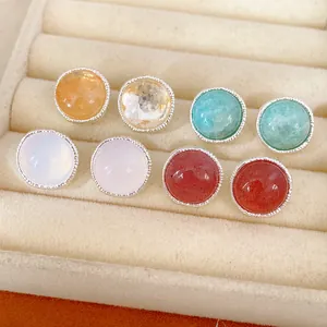 Close-up display of various colorful round gemstone stud earrings in a velvet jewelry tray