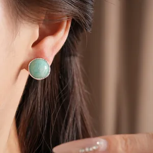 Macro view of a minimalist round green stone stud earring with textured silver bezel