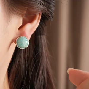 Detail view of a minimalist round light green stone stud earring worn on an ear with silver bezel