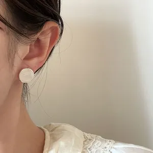 Close-up of a vintage-style round silver stud earring with white shell inlay on model