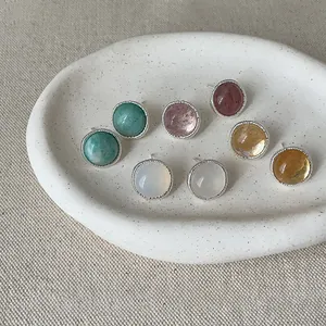 Detail of colorful round agate stud earrings with textured silver borders on white tray.