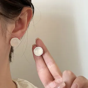 Close-up of elegant round silver needle earrings with white agate stone on ear and hand