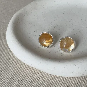 Close-up of vintage style round amber stone stud earrings on a white ceramic tray