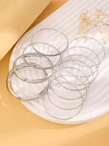 Vue rapprochée d'un ensemble de bracelets argentés superposés aux textures variées.
