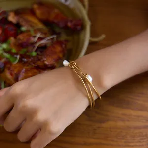 Elegant detail view of 18K gold plated stainless steel bangles with white pearls on wrist