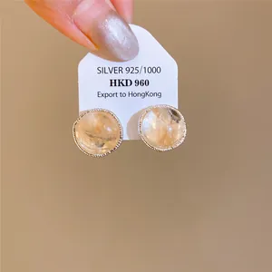 Detalle de pendientes redondos de ágata con borde dorado y aguja de plata.