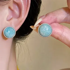 Detalle de pendientes redondos con piedras azul claro y metal en tono plateado.