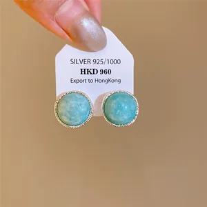 Detalle macro de pendientes redondos de piedra turquesa con tarjeta de plata ley 925