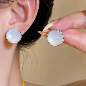 Primer plano de pendientes de ágata blanca con borde de plata en la oreja y la mano.