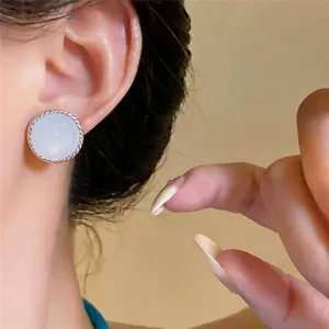 Elegantes pendientes redondos de ágata blanca con aguja de plata puestos en la oreja