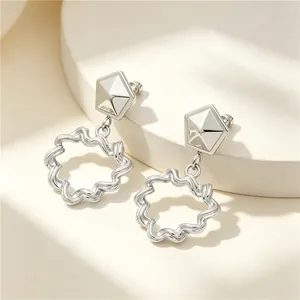 Close-up detail of silver stainless steel earrings with geometric studs and wavy hollow charms.
