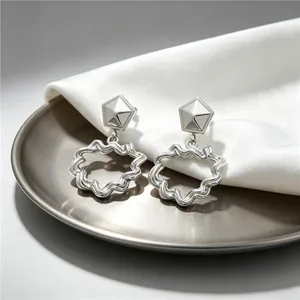 Detail shot of silver wavy hoop earrings with pleated texture on a white silk background.