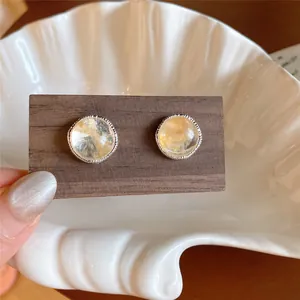 Detalle de pendientes de ágata redonda con aguja de plata y un borde con textura