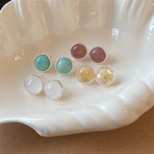 Detalle de pendientes de botón redondos con piedras de colores en una bandeja de cerámica.