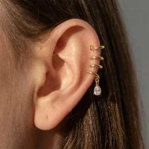 Close-up of a gold spiral ear cuff with a teardrop crystal drop on a model's ear.