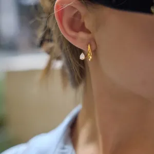 Détail d'une boucle d'oreille en acier doré avec un zircon en forme de poire