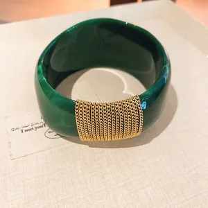 Macro detail of dark green marble-effect acrylic bangle with gold chain wrap