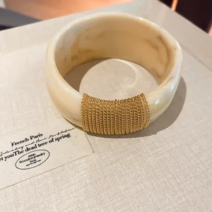 Close-up detail of a beige marble acrylic bangle featuring an elegant gold chain wrap