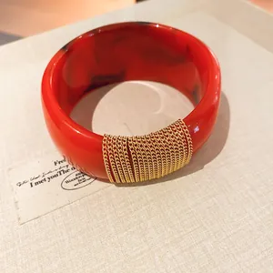 Close-up detail of a red gradient acrylic bangle featuring elegant gold chain wrap accents