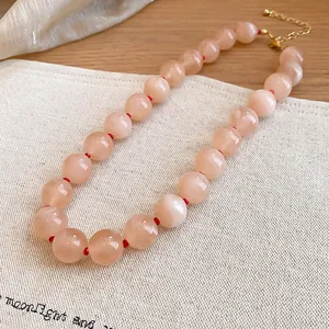 Primer plano de collar de cuentas acrílicas rosas con nudos rojos sobre lino.