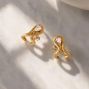 Primer plano de pendientes de acero de titanio dorado con circonita de gota sobre mármol