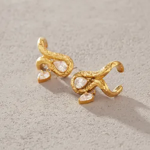 Primer plano de pendientes de acero dorado con brillantes circonitas en forma de pera.