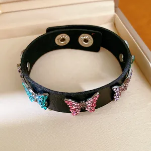 Détail d'un bracelet en cuir noir orné de breloques en forme de papillon en strass colorés